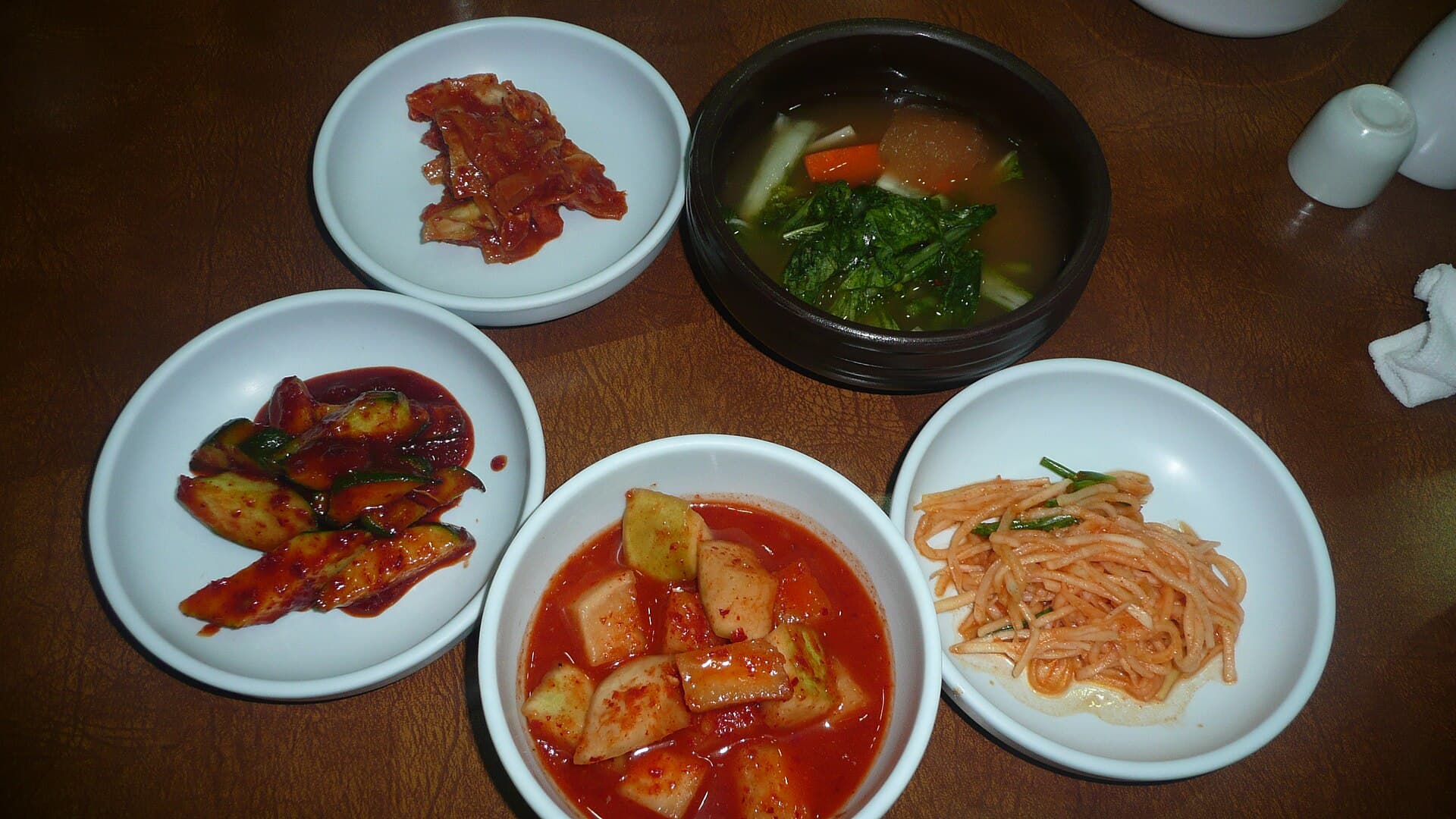 Cinq variétés de kimchi coréen présentées côte à côte dans des bols, illustrant la diversité des recettes traditionnelles à base de légumes fermentés.