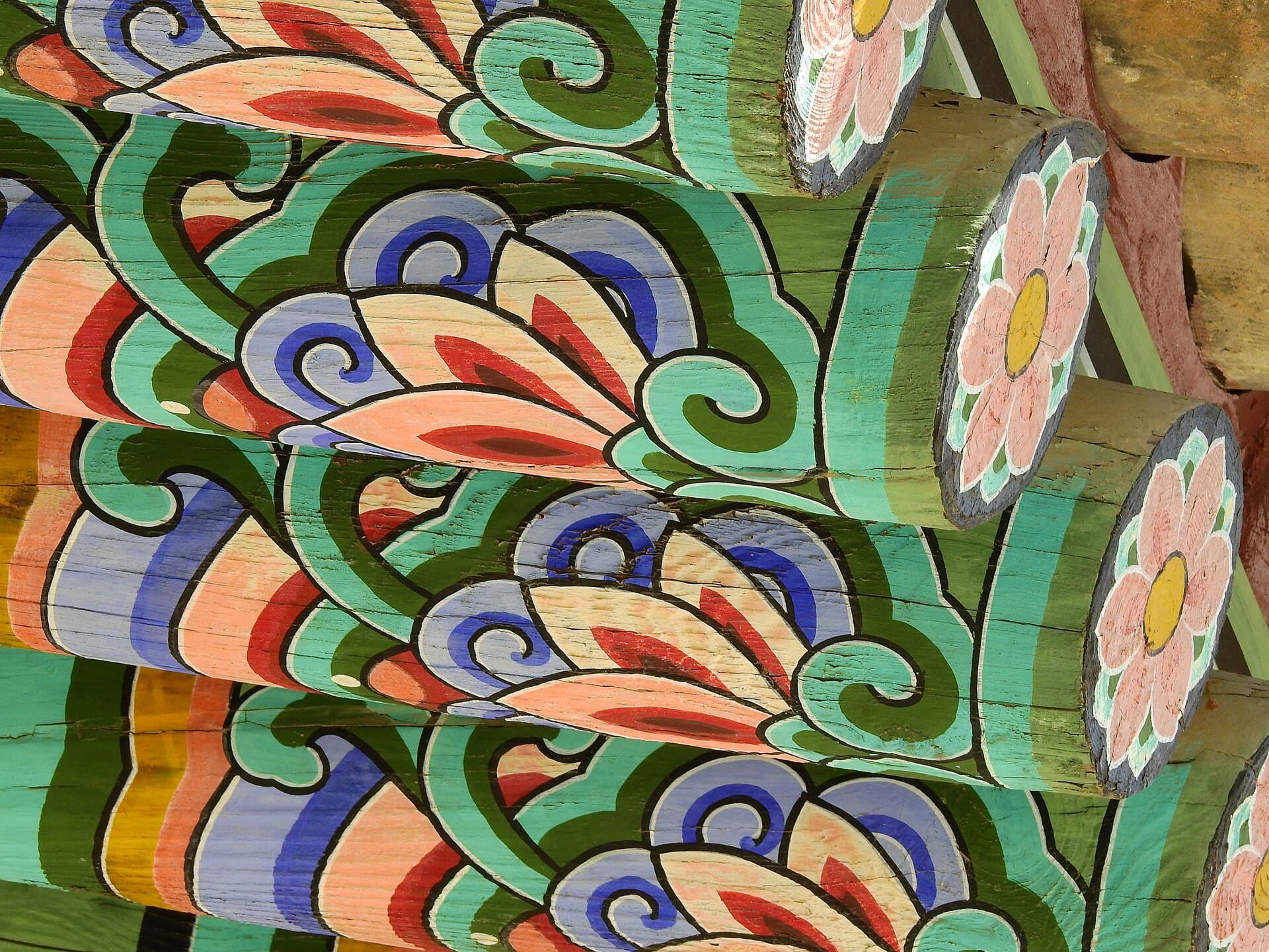 Gros plan sur le dancheong des avant-toits du palais Gyeongbokgung : chevrons peints de motifs floraux aux spirales bleues, vertes et rouges cernées de noir, ornées de lotus roses.