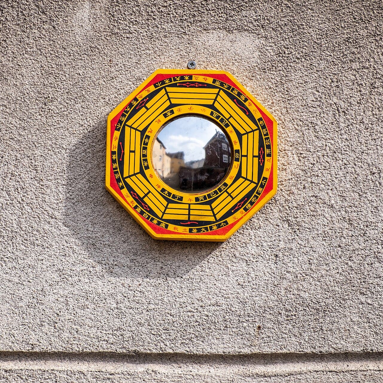 Miroir bagua octogonal jaune et rouge portant les huit trigrammes et un taijitu, fixé sur un mur