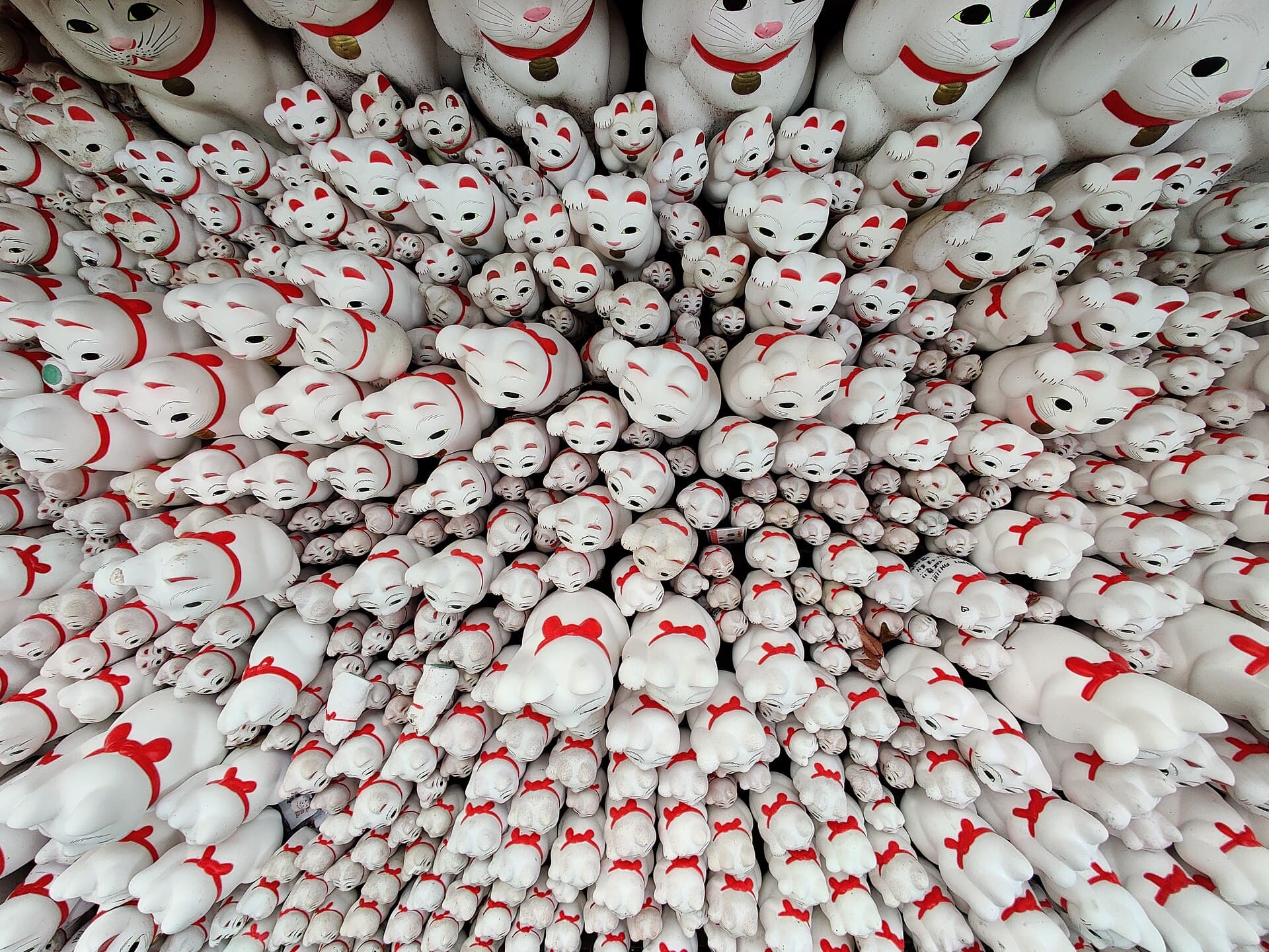 Centaines de figurines maneki-neko blanches, patte levée, alignées sur les étagères votives du temple Gōtoku-ji à Tōkyō.