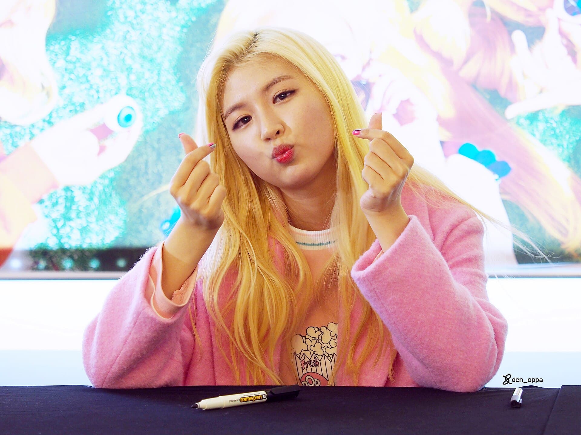 Une membre du girl group MyB fait le geste du « finger heart » (손하트), symbole de l'aegyo, le charme mignon si prisé de la culture pop coréenne.