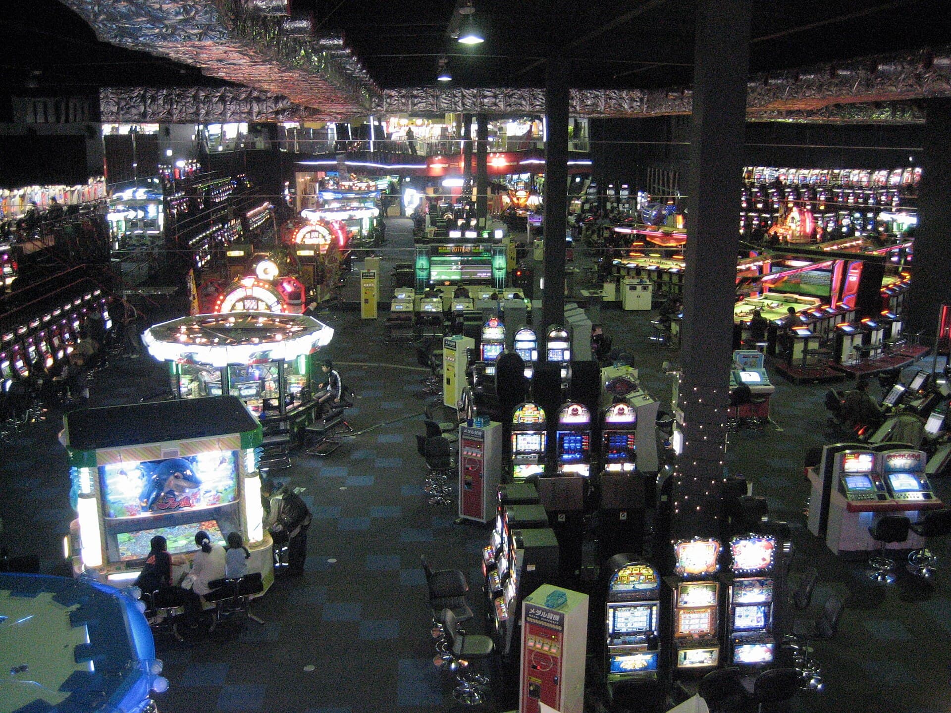 Vue plongeante sur l'interieur d'un game center japonais : rangees de bornes d'arcade, jeux a medailles et machines lumineuses