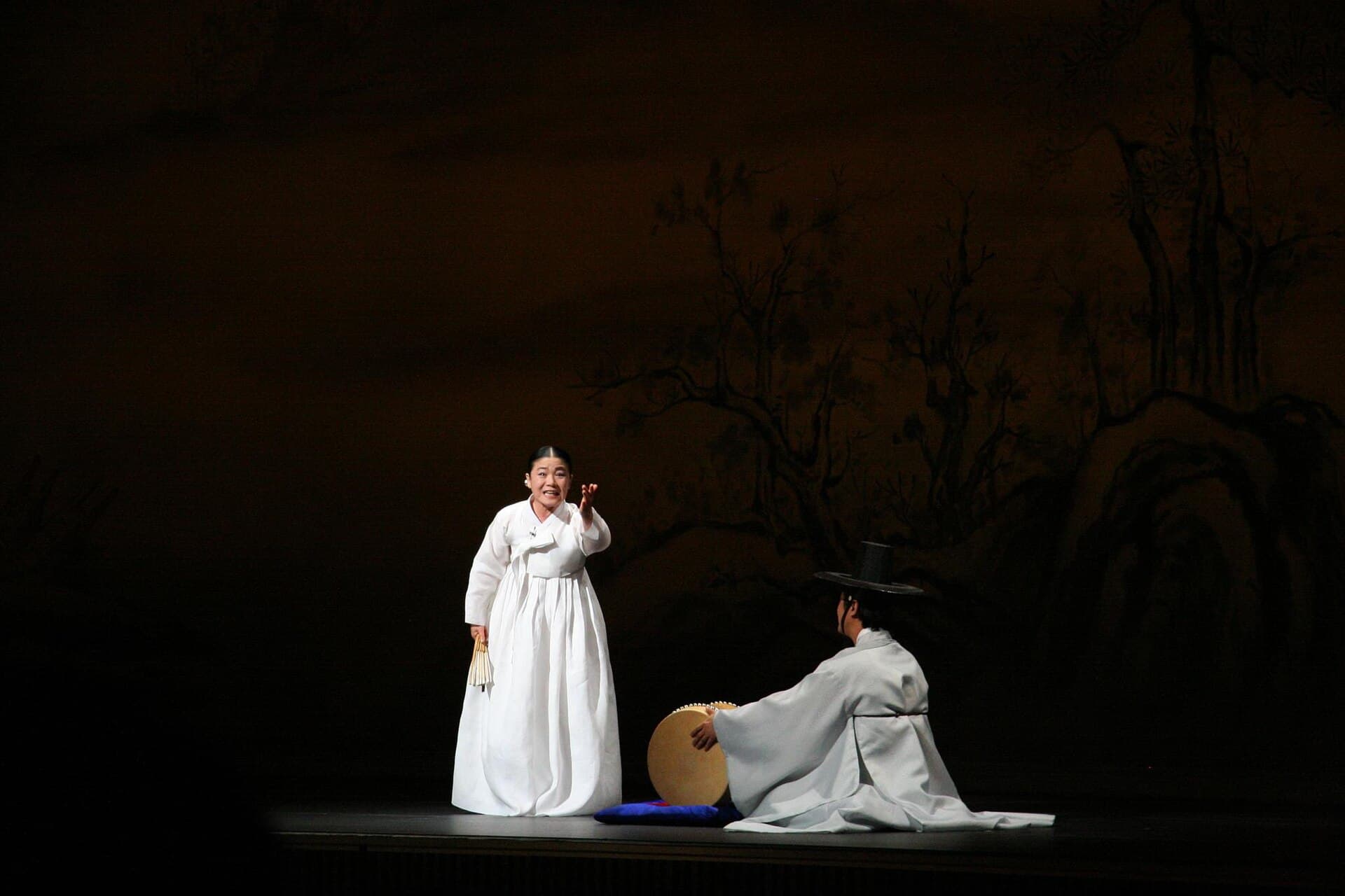 Chanteuse de pansori en hanbok tenant un éventail, accompagnée d'un joueur de tambour buk lors d'une performance traditionnelle coréenne