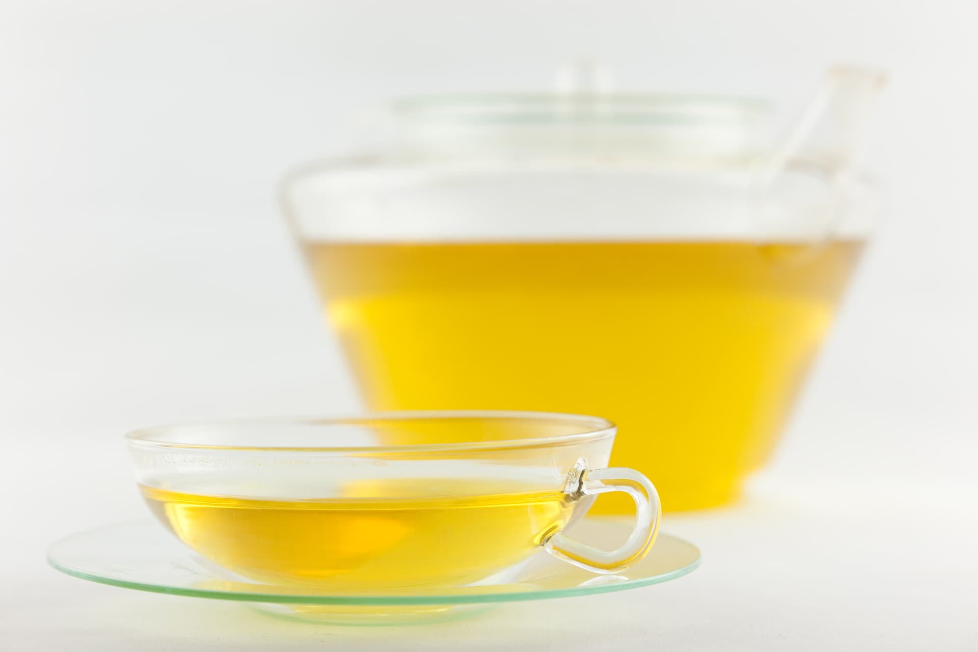 Thé vert japonais sencha fraîchement infusé, servi dans une tasse avec sa théière en verre assortie, révélant la teinte vert doré caractéristique de l'infusion.