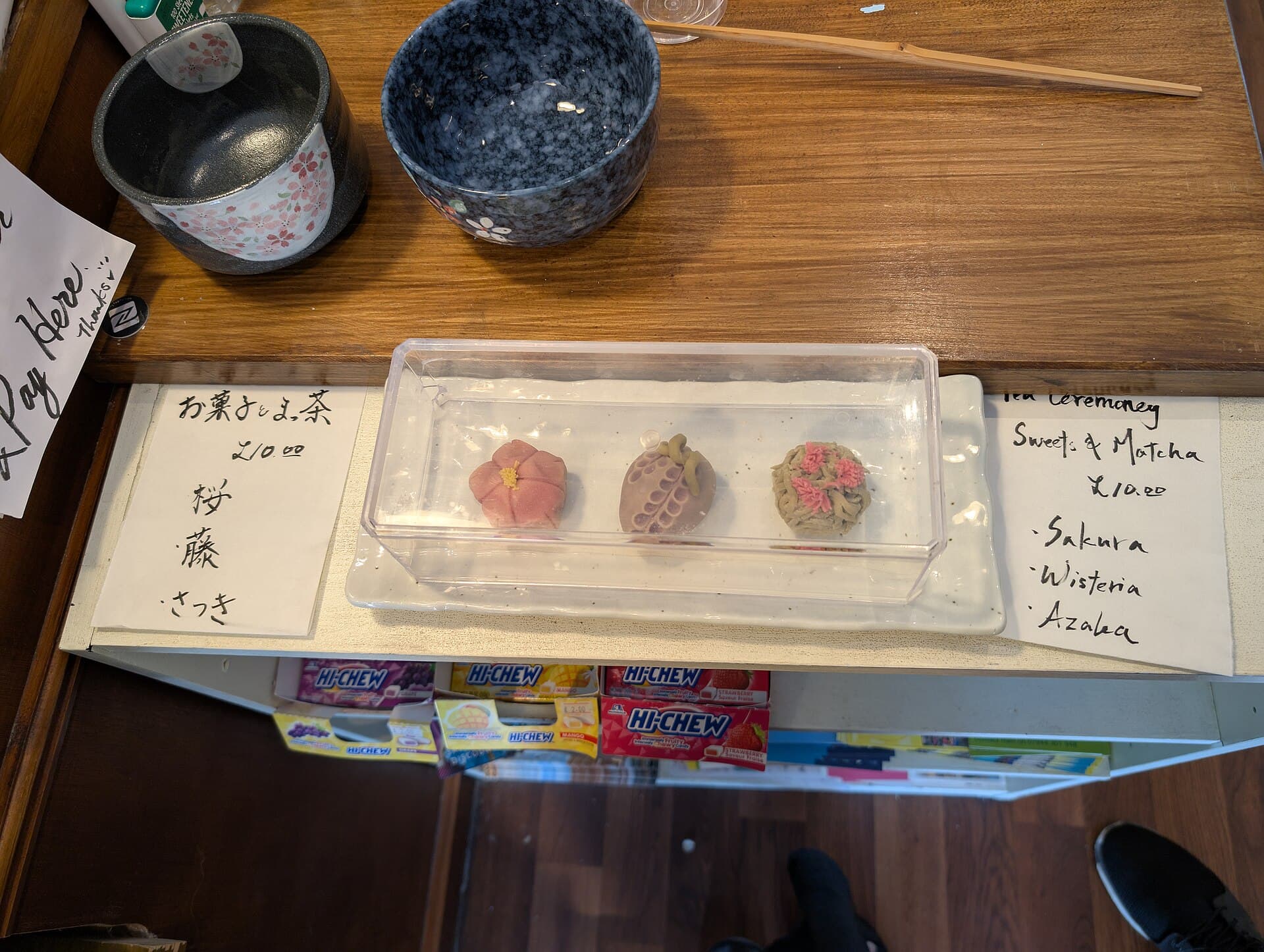 Trois wagashi nerikiri colorés en forme de fleurs (sakura, glycine et azalée) disposés en rangée, illustrant la finesse artisanale de la pâtisserie traditionnelle japonaise.
